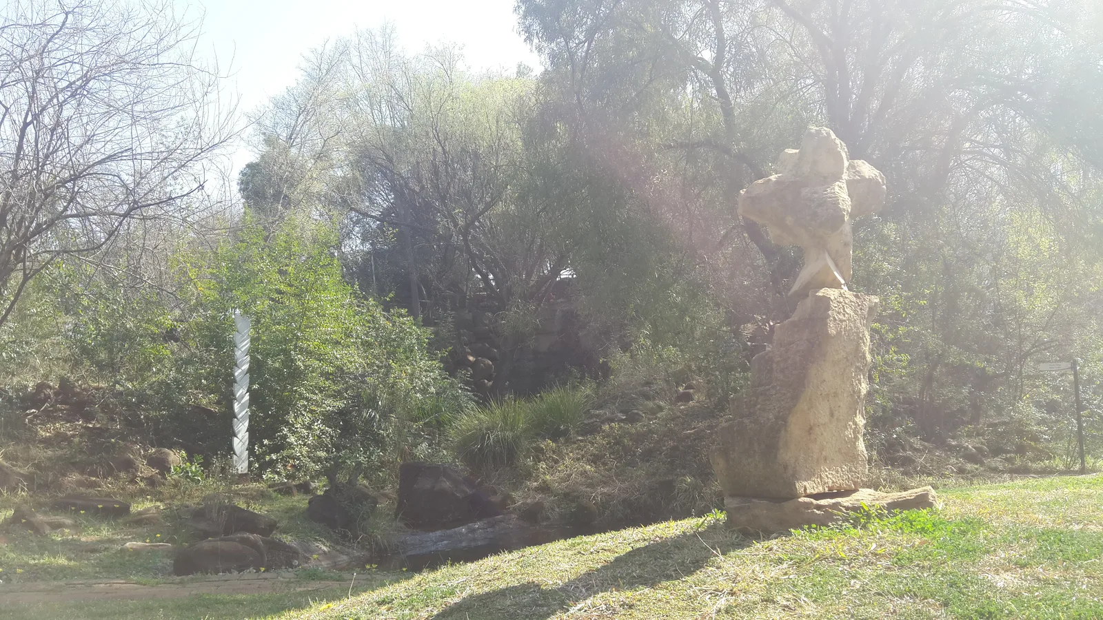 Sunlit indigenous garden and stone sculpture at the NWU Botanical Garden in Potchefstroom.